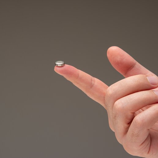 Small medical device battery sitting on the index finger of a man