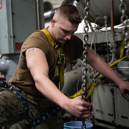 U.S. Navy Aviation Boatswain’s Mate heaves a chain from the hangar bay of the aircraft carrier USS John C. Stennis (CVN 74).