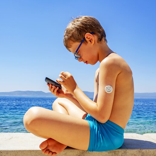 Boy with wearable medical device sitting on a beach playing on his phone