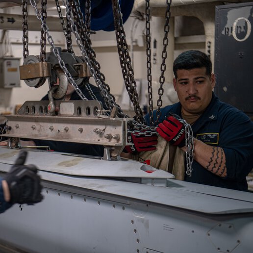 Sailors hoist an ordnance shell aboard an aircraft carrier (CVN 68).