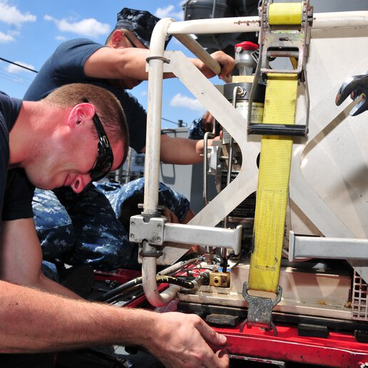 Sailors on the submarine tender USS Emory S. Land (AS 39) repair air compression equipment.