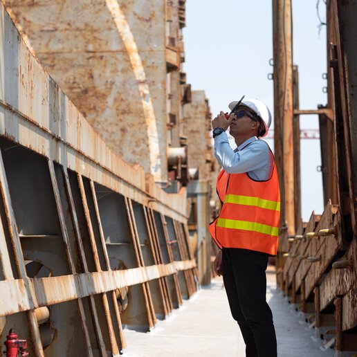 Marine foreman speaking into a walkie talkie wearing a safety vest and hard hat.