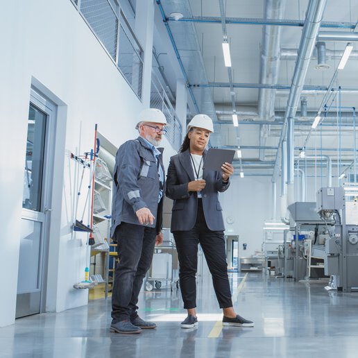 Two manufacturing employees in hard hats near manufacturing equipment.